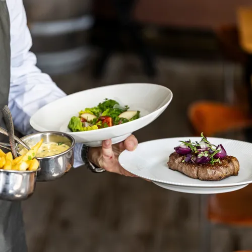 tjener servere bøf med bearnaise og salat.webp